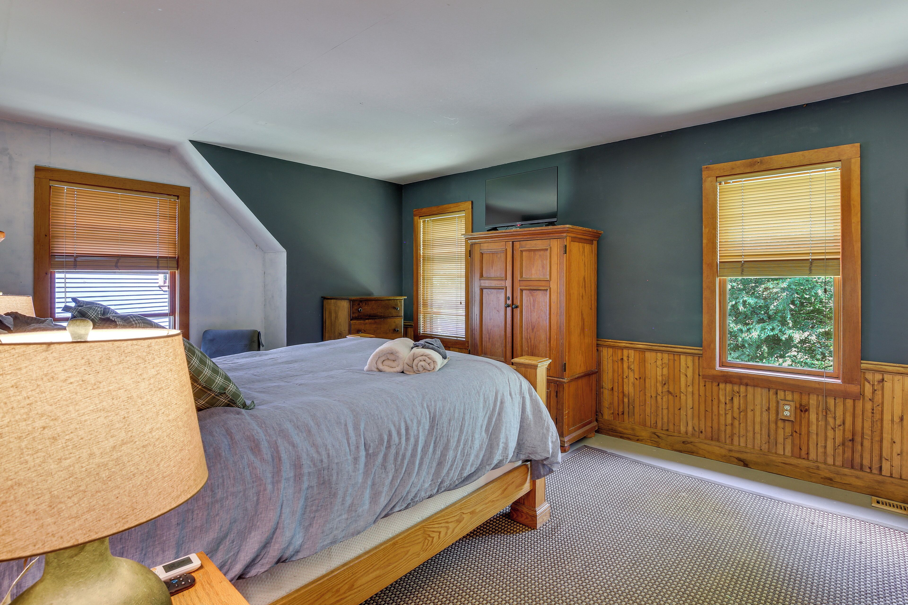 A bedroom with a bed, a nightstand, a lamp, a dresser, and a window with blinds.