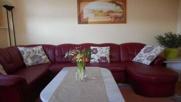 Ein rotes Ledersofa mit Blumenkissen, eine Vase mit Blumen und ein Bild an der Wand.