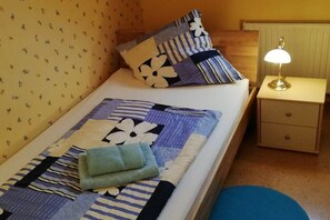 A neatly made bed with a floral and striped bedspread, a pillow with a similar pattern, a bedside lamp, and a small bedside table with a drawer. - Holiday apartment with 3 bedrooms (Lauterbach)