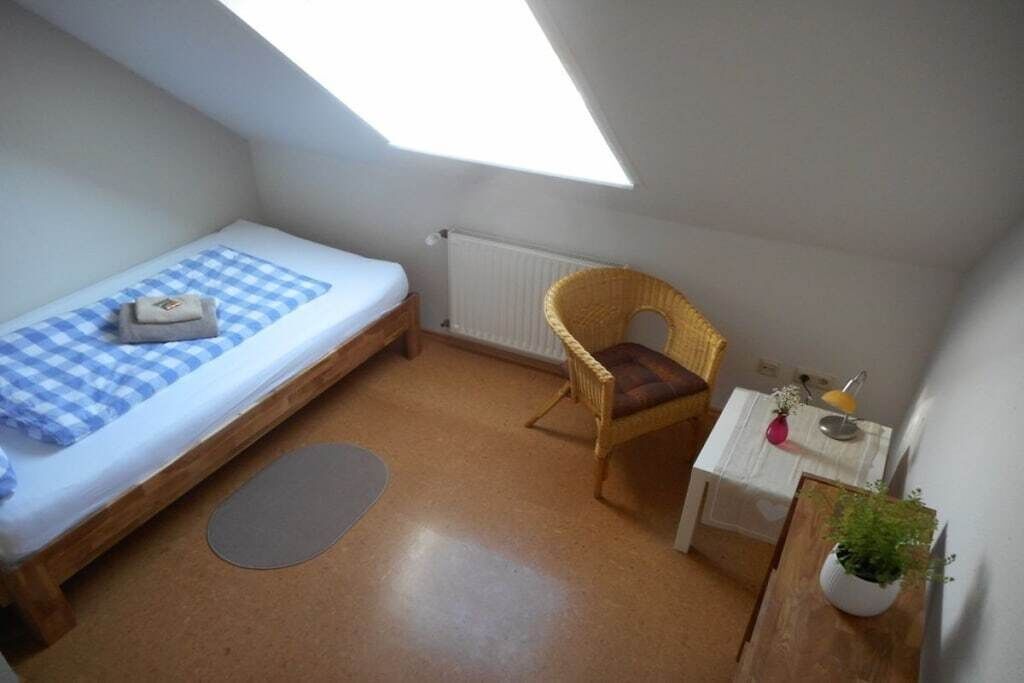 Een kleine, compacte kamer met een eenpersoonsbed, een stoel, een tafeltje en een radiator.