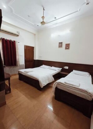 A hotel room with two beds, a wooden headboard, a ceiling fan, and a red curtain. - Shubh Inn Jodhpur (Jodhpur)