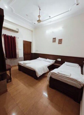 A hotel room with two beds, a wooden headboard, a ceiling fan, and a red curtain. - Shubh Inn Jodhpur (Jodhpur)