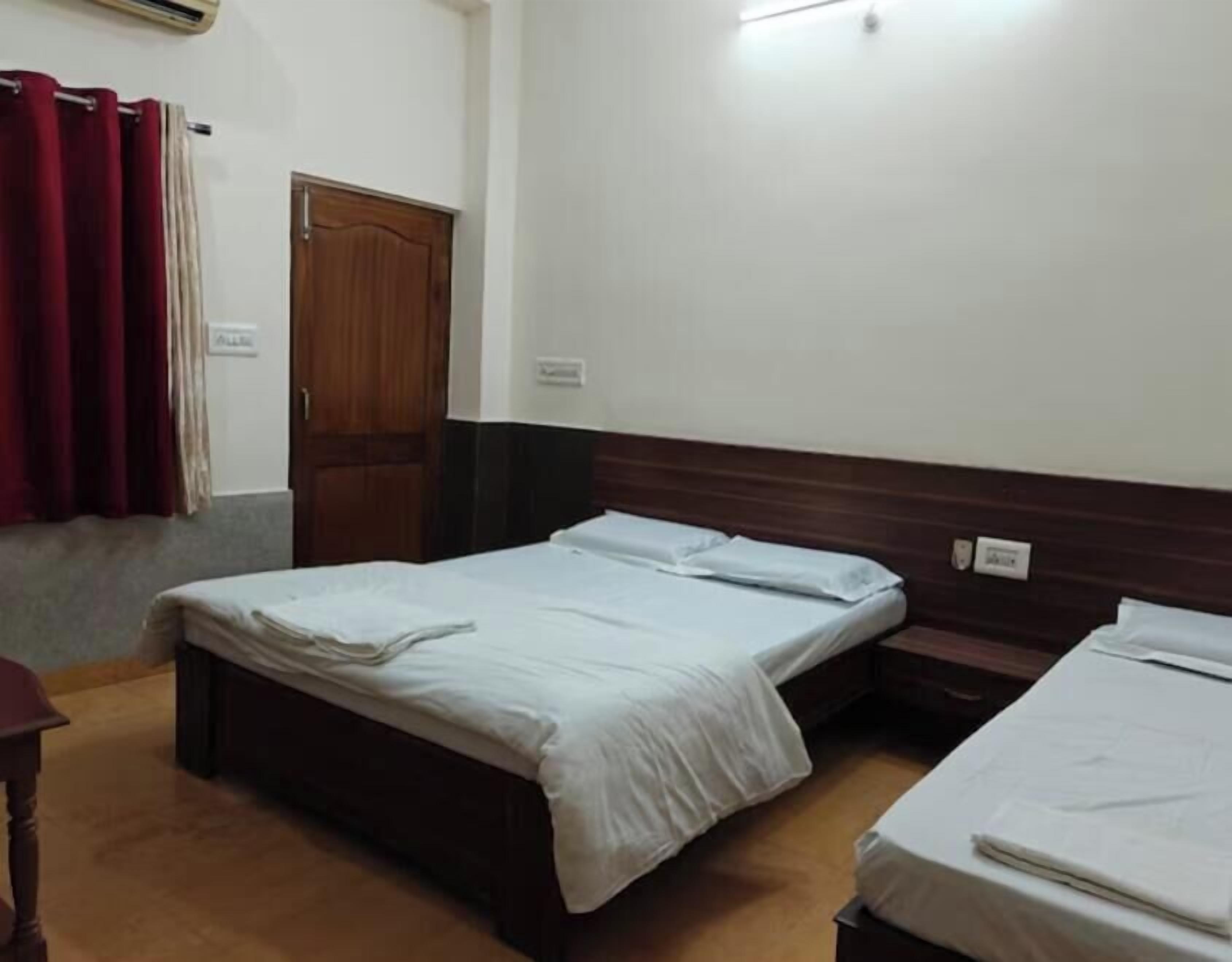 A hotel room with a single bed, a wooden headboard, a wooden door, and a red curtain.