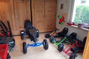Een kamer met houten kasten, een raam met uitzicht, en meerdere kinderloopfietsen.