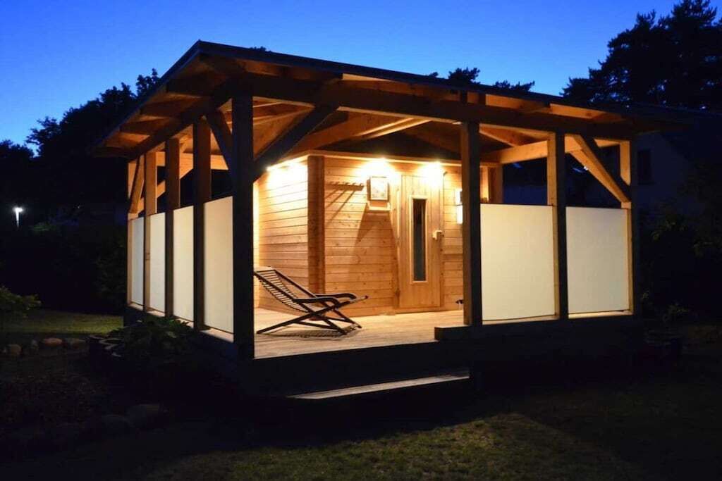 Una cabaña de madera con un porche cubierto y una sola silla de descanso.
