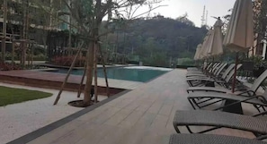 A poolside area with lounge chairs and umbrellas, surrounded by trees and a view of a hill. - Cozy condo near walking street pattaya (ตำบล หนองปรือ)