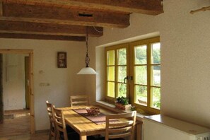 Een eethoek met een houten tafel en stoelen, een hanglamp en een raam met uitzicht op groen.