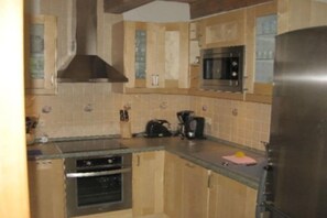 Eine Küche mit Holzausstattung, einem Edelstahlkühlschrank, einer Mikrowelle und einem Backofen.