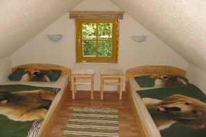 Een kleine, driehoekige slaapkamer op zolder met twee bedden, elk voorzien van een beddegoed met hondjesprint, een raam en een houten vloer.
