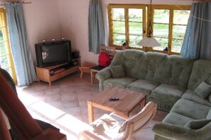 Een woonkamer met een televisie op een houten dressoir, een groene bank, een houten salontafel en een raam met gordijnen.