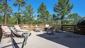 A covered outdoor seating area with lounge chairs and a table, surrounded by a wooden fence and tall pine trees. - 1 Mi to Courthouse Plaza! Home w/ Deck + Fireplace (Prescott)