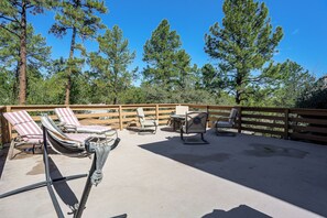 A covered outdoor seating area with lounge chairs and a table, surrounded by a wooden fence and tall pine trees. - 1 Mi to Courthouse Plaza! Home w/ Deck + Fireplace (Prescott)