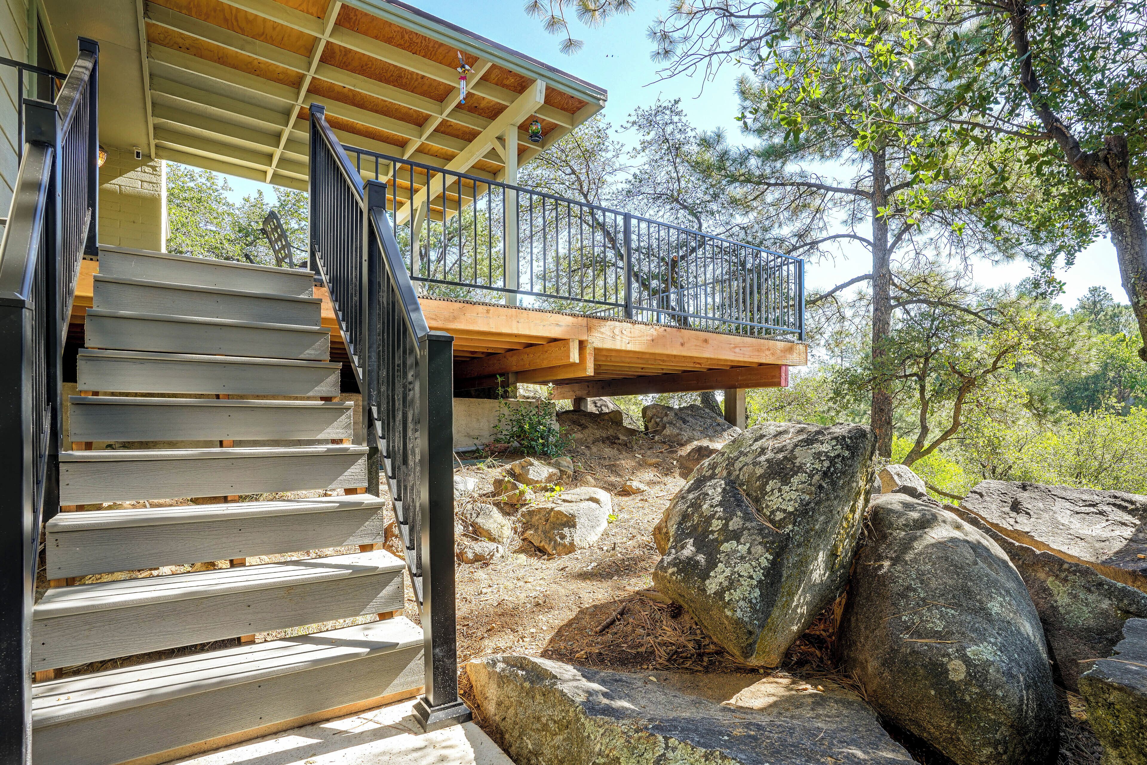 A wooden staircase leading to a balcony with a metal railing, surrounded by natural scenery and large rocks.