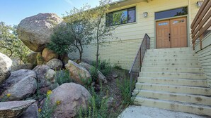 A building with a yellow exterior, a wooden staircase, and large rocks in the foreground. - 1 Mi to Courthouse Plaza! Home w/ Deck + Fireplace (Prescott)