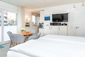 A hotel room with a bed, a dining table with chairs, a kitchen area, and a TV mounted on the wall. - Apartment in Juist with swimming pool (Juist)