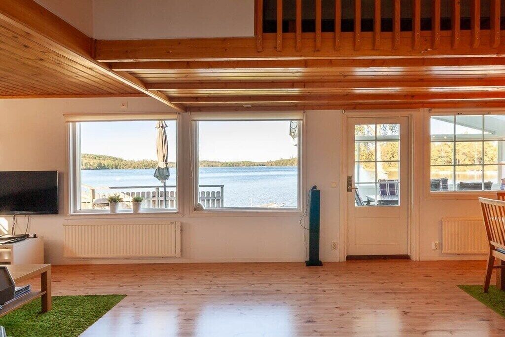A spacious room with large windows, a wooden ceiling, and a view of a lake.