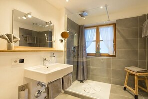 A modern bathroom with a sink, mirror, shower, and a small stool. - Holiday apartment with 1 bedroom (Obermaiselstein)