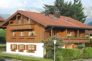 A wooden chalet with a sloped roof, multiple windows, and a balcony. - Holiday apartment with 1 bedroom (Obermaiselstein)