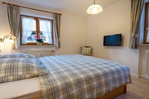 A bedroom with a bed, a television, a window with curtains, and a radiator. - Holiday apartment with 1 bedroom (Obermaiselstein)