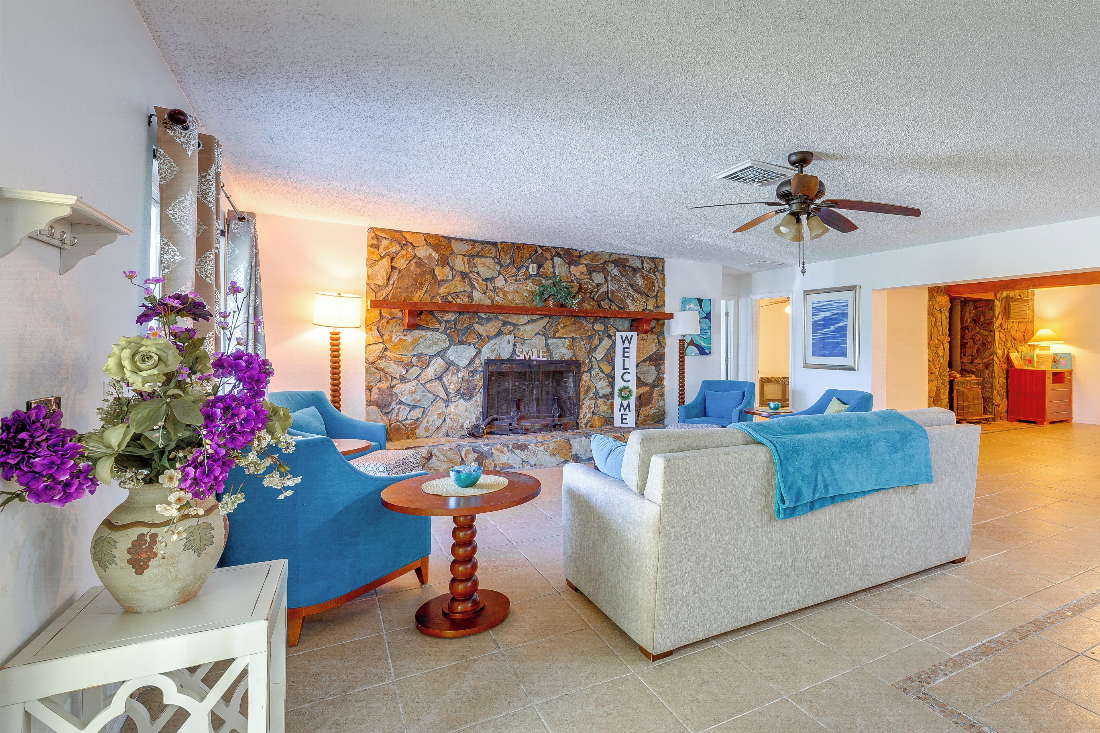 A living room with a stone fireplace, blue sofas, a coffee table, and a ceiling fan.