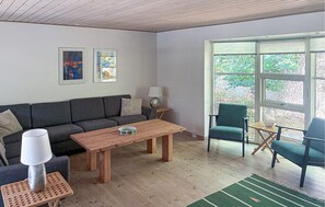 A modern living room with a sofa, a coffee table, a lamp, and a chair. There are two framed artworks on the wall and a large window with a view of greenery. - Stunning home in Store Fuglede with sauna (Store Fuglede)
