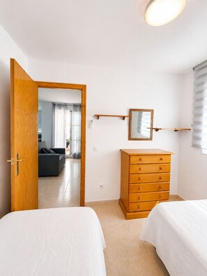 A bedroom with a wooden dresser, a bed, a mirror, and a door leading to a living area. - residencial portofino VI oropesa ref 081 (Oropesa del Mar)