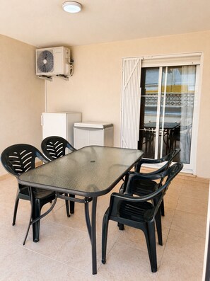 A balcony with a table and chairs, an air conditioning unit, a refrigerator, and a sliding glass door leading to an outdoor area. - residencial portofino VI oropesa ref 081 (Oropesa del Mar)
