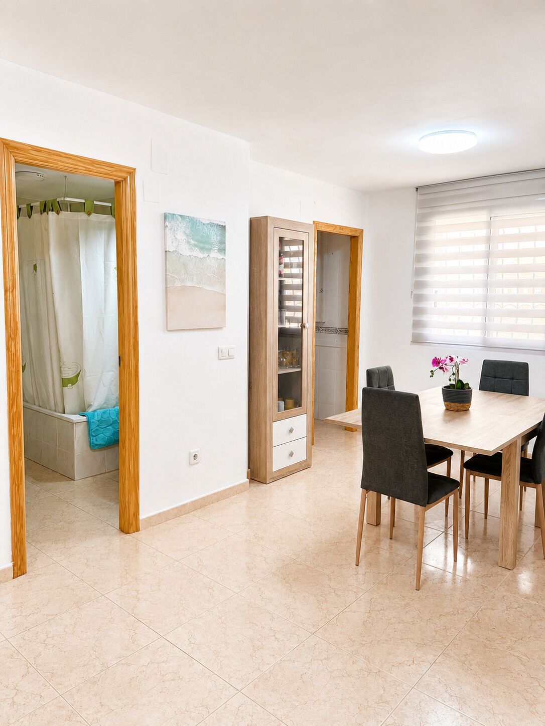 A room with a dining table, chairs, a shower area, and a cabinet with drawers.
