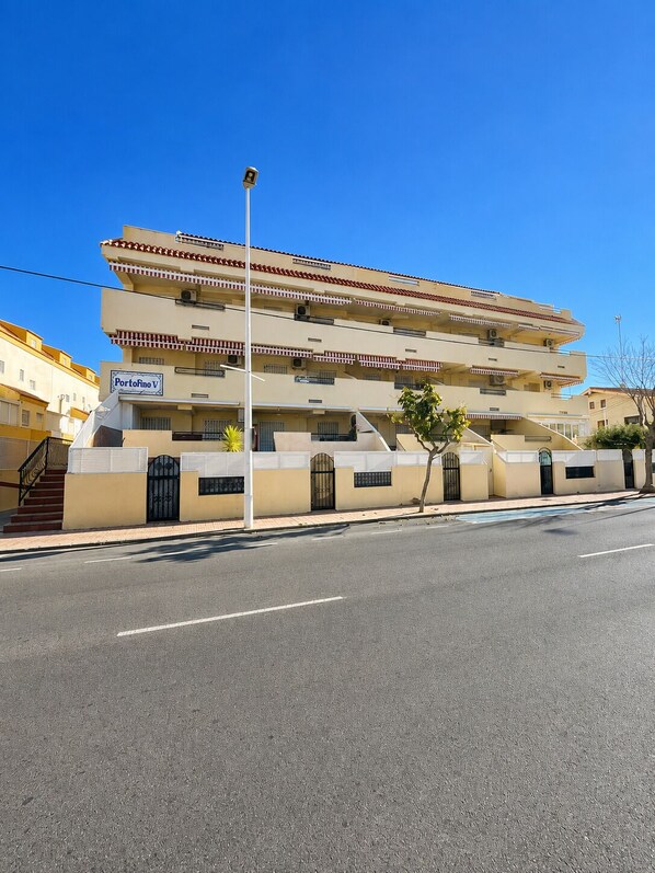 A multi-story building with a flat roof, a visible entrance with a gate, and a clear sky. - residencial portofino VI oropesa ref 081 (Oropesa del Mar)