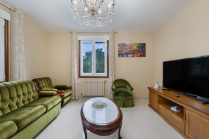 A living room with a green sofa, a round coffee table, a television on a wooden stand, and a painting on the wall.