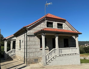 A stone building with a red-tiled roof, a balcony, and a staircase leading to the entrance.