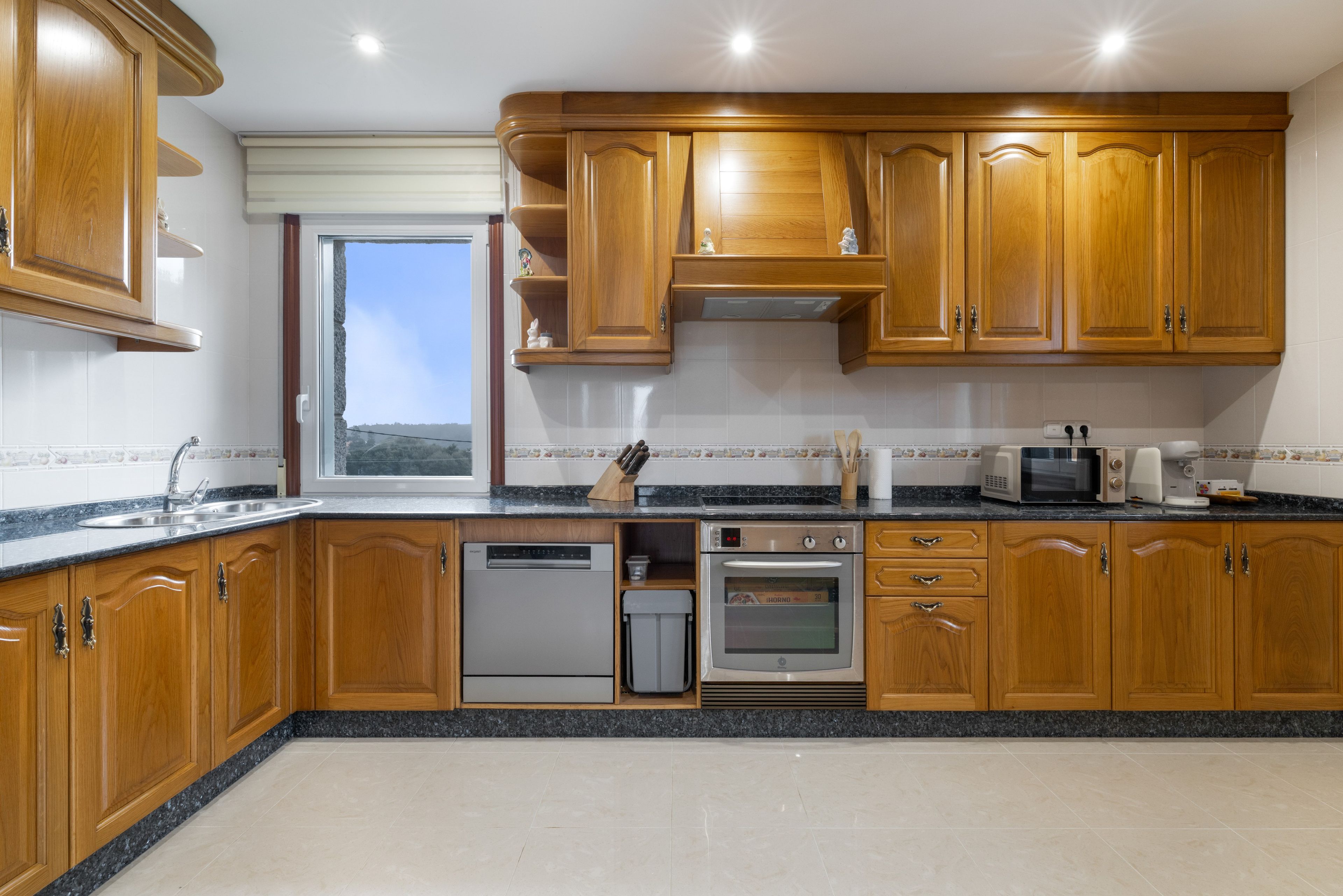 Una cocina con armarios de madera, lavavajillas, horno y ventana con vistas.