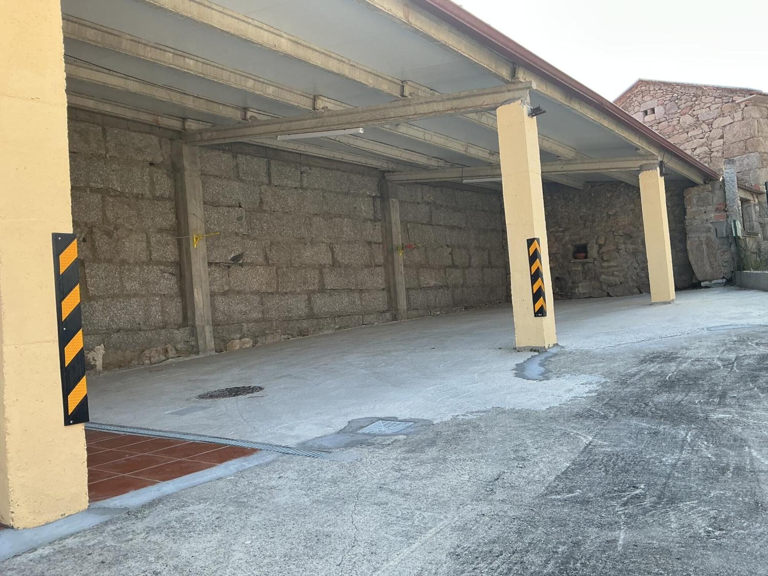 Un garaje para estacionar con pilares de hormigón y suelo de baldosas.