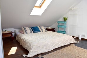 A bedroom with a skylight, a bed with patterned bedding, a teal side table, a white radiator, and a hanging plant. - Rooftop terrace loft apartment, home cinema (Praha 10)