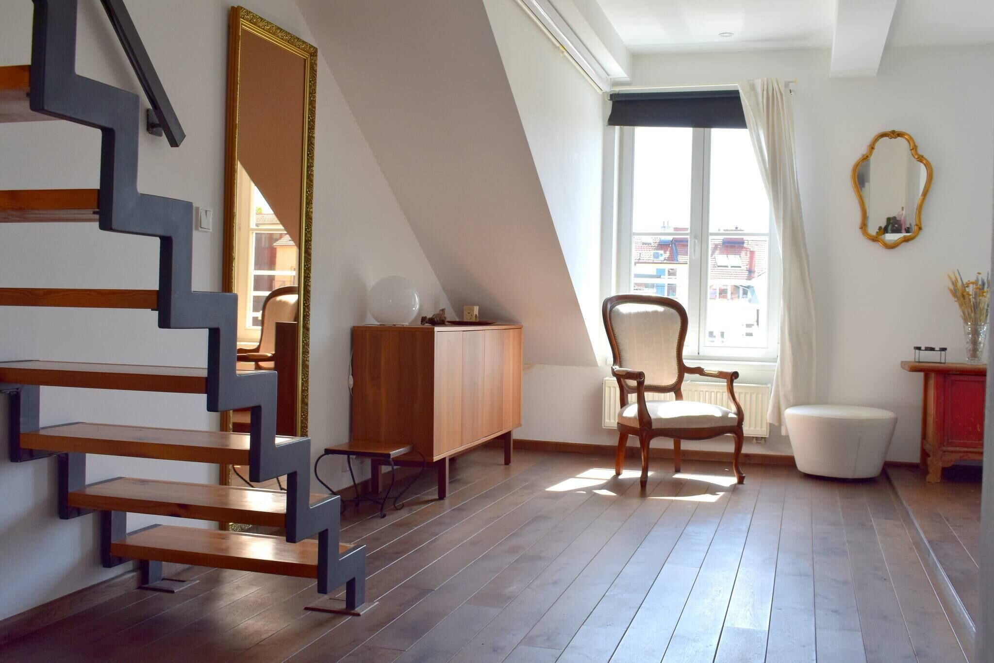 A room with a modern staircase, a wooden cabinet, a chair, a radiator, and a window with curtains.
