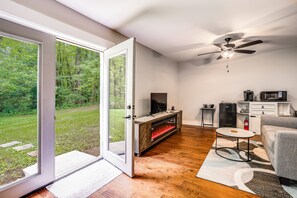 A room with a sliding glass door leading to a grassy yard, a fireplace, a ceiling fan, a small table, and a sofa. - Hilltop Studio Hideaway Near Chattanooga (Middle Valley)