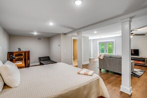 A spacious bedroom with a large bed, a wooden nightstand, a desk with a lamp, and a view of a living area with a sofa and a fireplace. - Hilltop Studio Hideaway Near Chattanooga (Middle Valley)