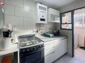 Una cocina moderna con estufa a gas, horno y microondas. Cuenta con una ventana con vistas al exterior, y armarios blancos y encimera de granito.