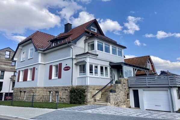 Une maison à deux étages, avec des fondations en pierre, un garage et un escalier apparent menant à l’entrée.