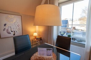 Une chambre d’hôtel équipée d’une table à manger, de deux chaises, d’une lampe, d’une œuvre d’art encadrée et d’une fenêtre donnant sur des panneaux solaires et un paysage enneigé.