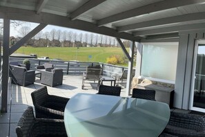 Un espace extérieur aménagé en terrasse, avec des meubles en osier, une table en verre et une vue sur un champ verdoyant.