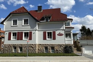 Un bâtiment à deux étages, avec une base en pierre, un toit recouvert de tuiles rouges et une enseigne indiquant « HARZER FLUR ».