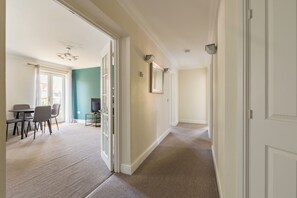 A hallway with carpeted flooring, a dining area with a table and chairs, and a television. - Green Light in Brondesbury Park (London)