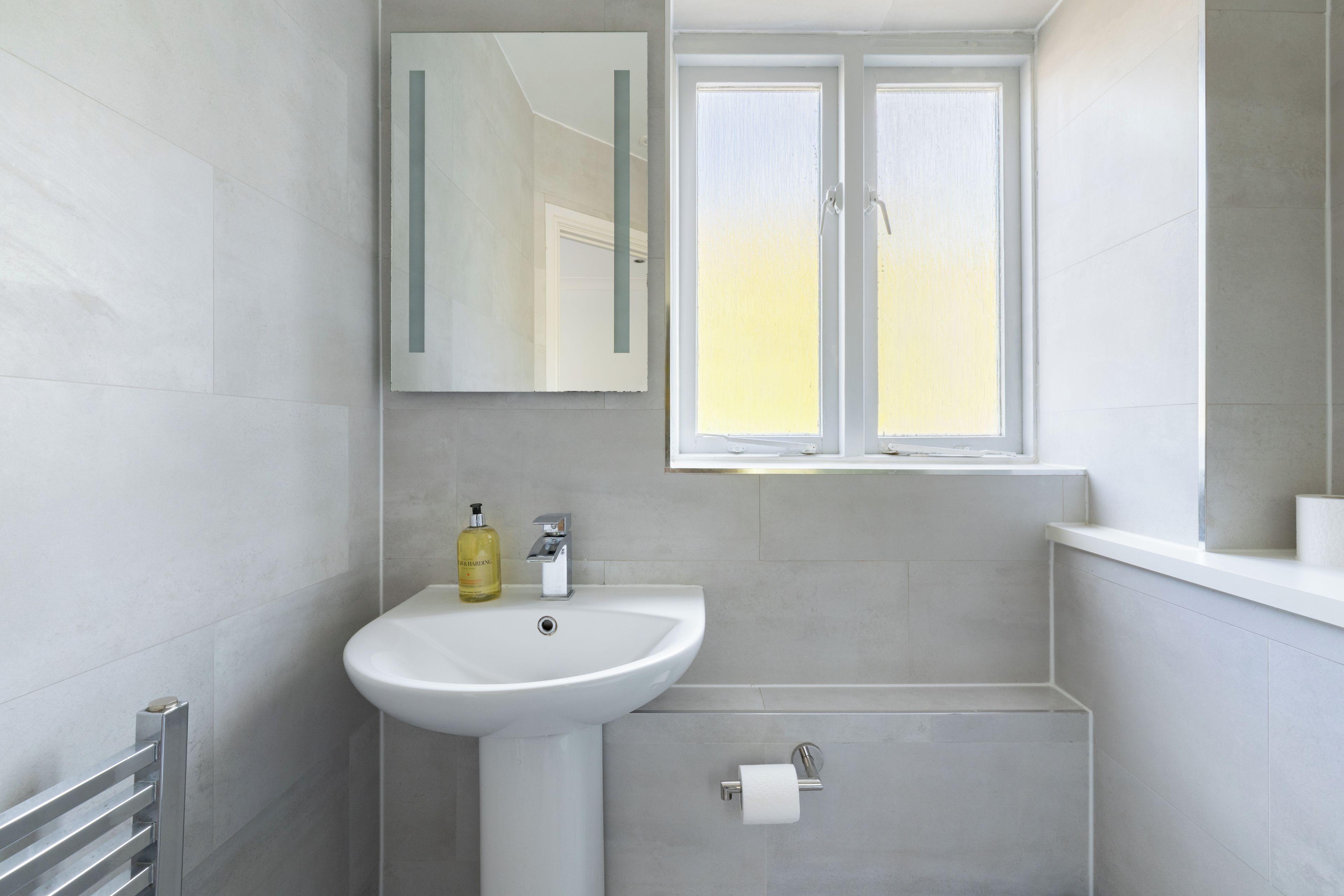 Ein modernes Badezimmer mit einem weißen Waschbecken, einem Spiegel und einem Fenster.