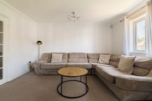 A corner living room with a beige sectional sofa, a round coffee table, a floor lamp, and a ceiling light fixture. - Green Light in Brondesbury Park (London)