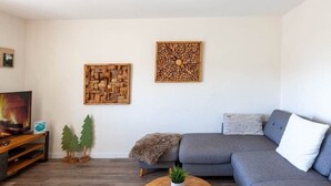 Sala de estar com um sofá cinza, uma mesa de centro de madeira com uma planta, e duas obras de arte na parede.