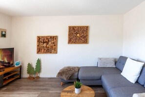 A living room with a grey sofa, a wooden coffee table with a plant, and two wall art pieces. - Holiday apartment with 2 bedrooms (Braunlage)