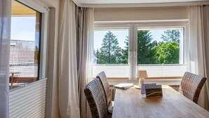 Quarto com mesa de jantar, duas cadeiras e janela com cortinas.