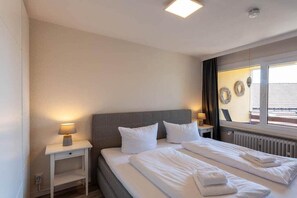 A hotel room with a bed, bedside tables, a window with curtains, and wall decorations. - Holiday apartment with 2 bedrooms (Braunlage)