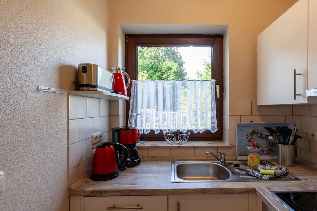 Eine kleine Küche mit Fenster, Spüle und diversen Geräten.